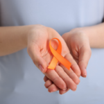 Person holding an orange multiple sclerosis awareness ribbon in support of MS wellness and symptom management.